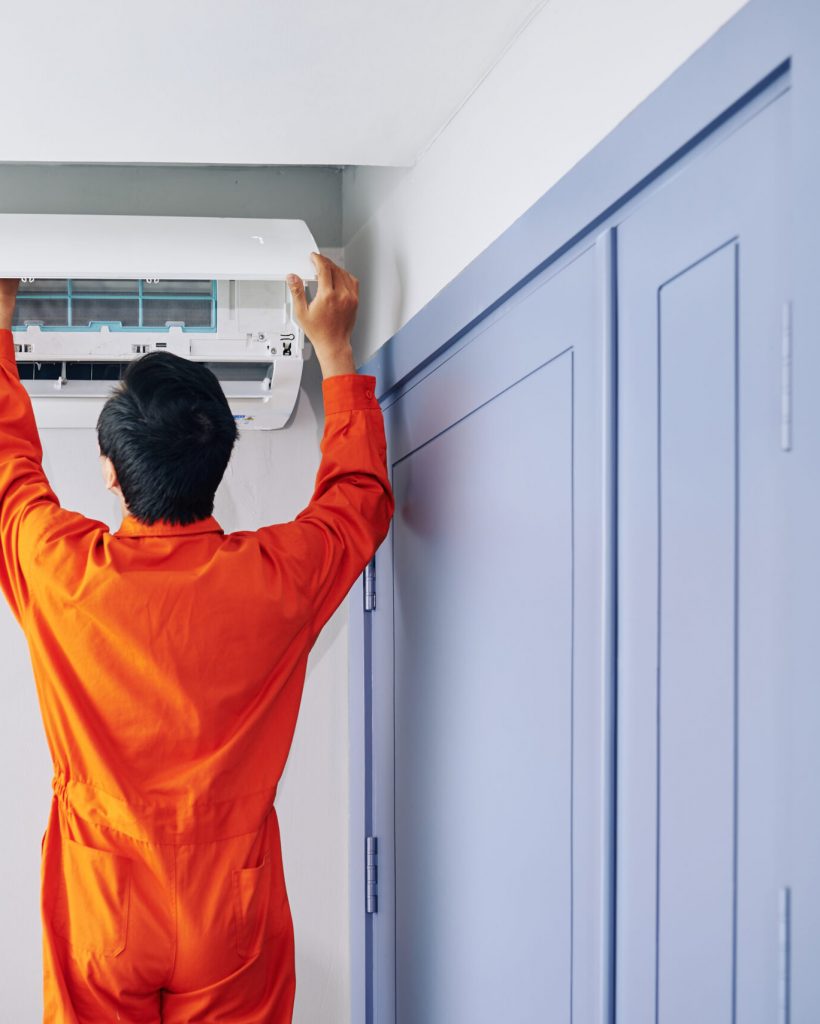 Service worker installing air conditioner in house, view from the back